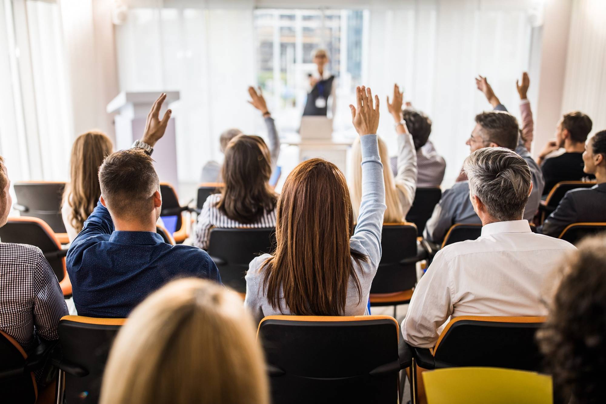People at a conference, some raising their hands, and a conference speaker